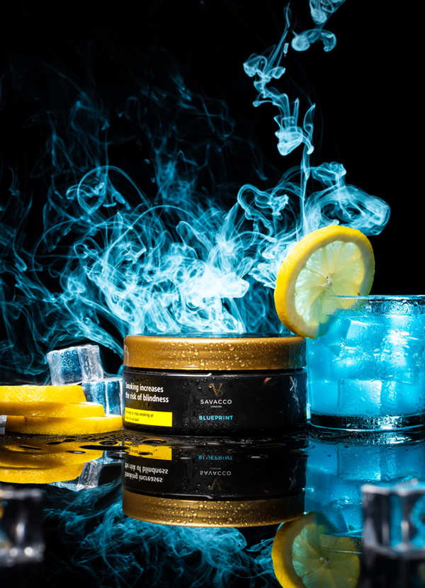 Shisha tobacco tin with lemon slices, blue cocktail, ice cubes, and swirling smoke on black